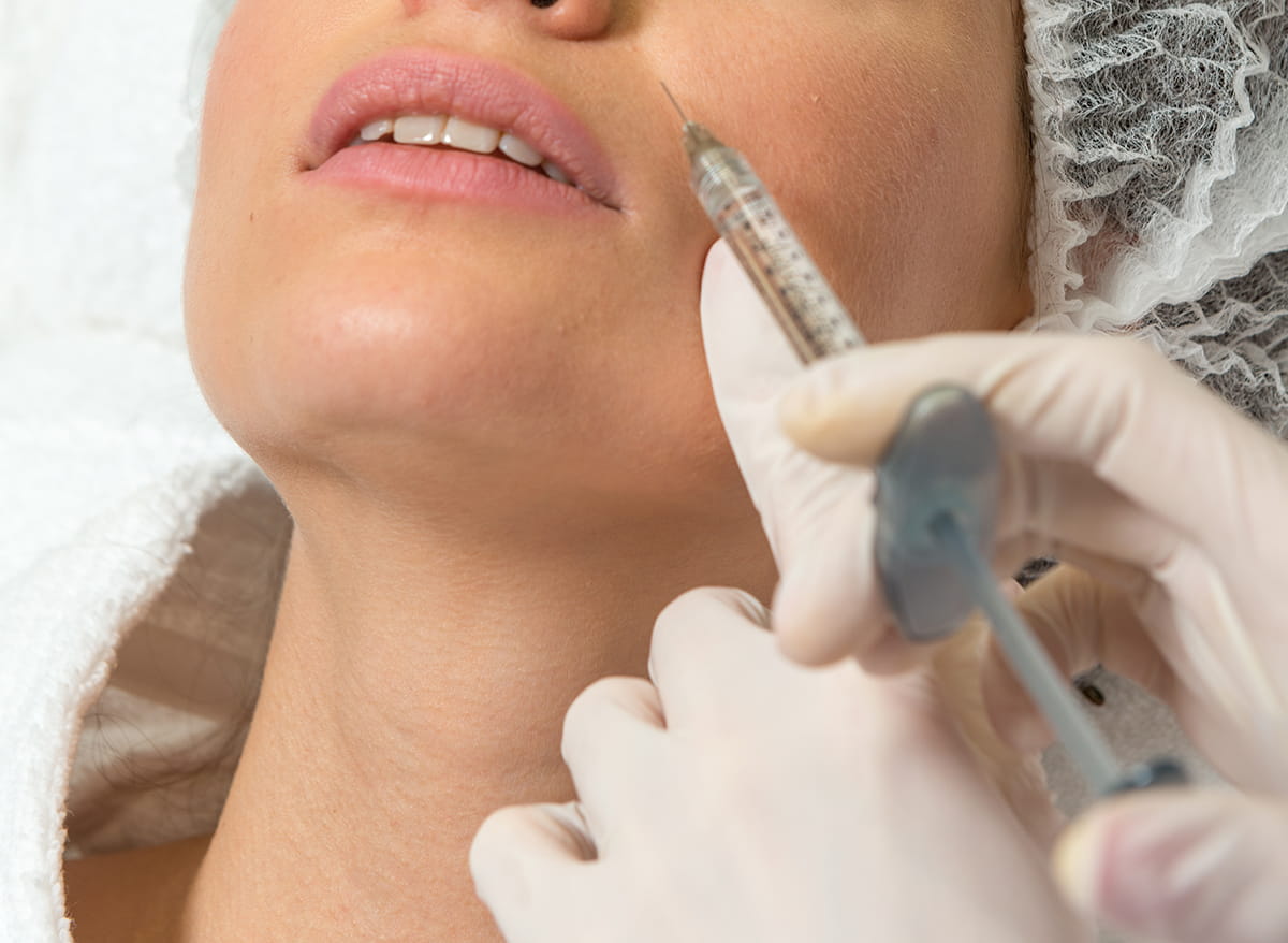 Femme recevant une injection cosmétique aux lèvres dans un spa médical, gros plan sur la seringue près de la bouche et du menton, traitement de dermatologie esthétique.